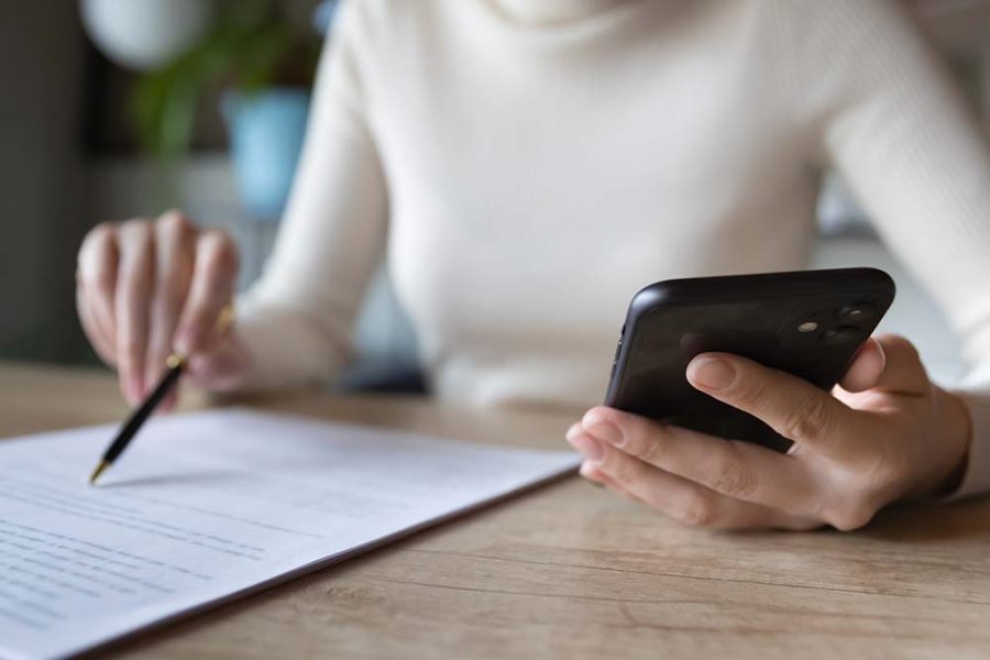 A person looking at a paper document whilst holding a smartphone in the other hand