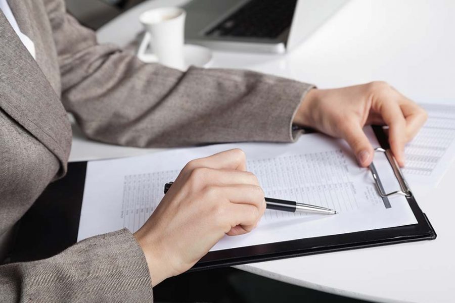 A person pointing a pen at an entry on a clipboard