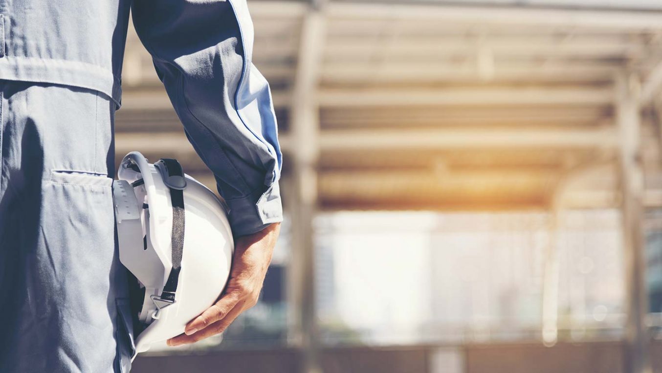 A person holding a hard hat against their hip