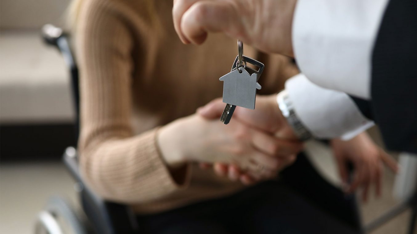 A person shaking hands with one hand holding house keys in the other hand