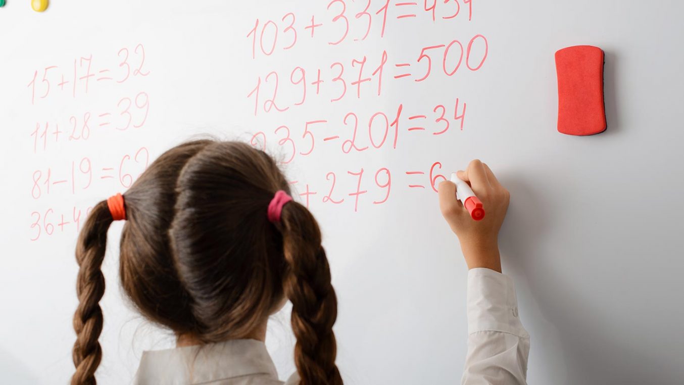 A child writing the answer to a maths sum on a whiteboard