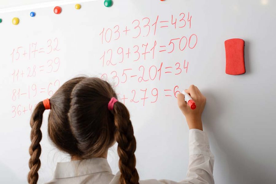 A child writing the answer to a maths question on a whiteboard