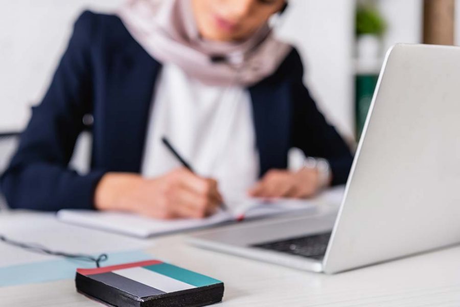 A person making notes in a notebook looking at a laptop