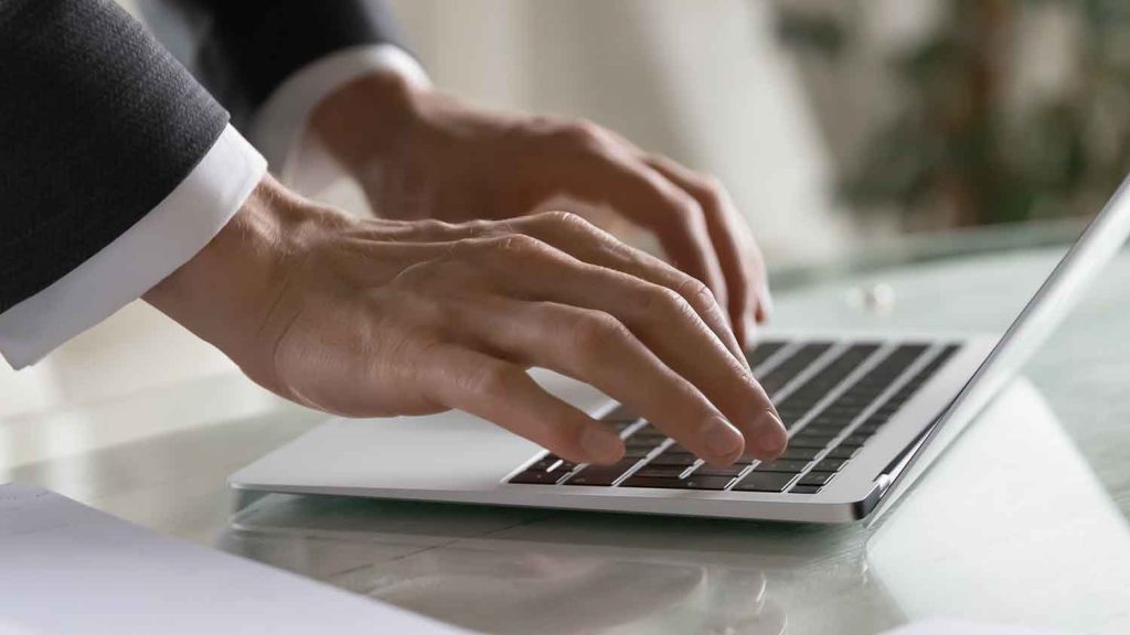 Persons hand on the keyboard of a silver laptop, poised to type