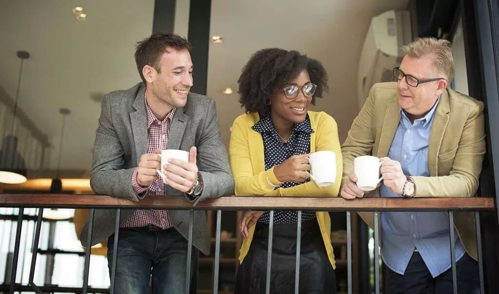 Three people having a drink whilst leaning over a balcony