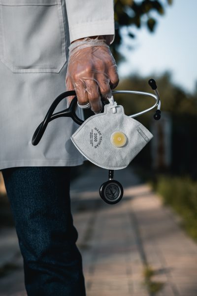 A doctor wearing plastic gloves, carrying a mask and stethoscope